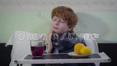 悲伤的白种人红头发的孩子，流感，<strong>拿起杯子</strong>喝茶，就像坐在床上一样。 可爱的不安不健康的孩子